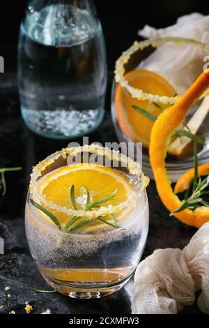 Eau Tonique cocktail avec le romarin et d'orange. Deux verres et la bouteille avec le sucre le zeste et de bulles sur fond texture noire. Une boisson rafraîchissante Banque D'Images