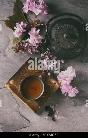 Fer noir, théière et tasse de thé en céramique traditionnel en bois servant de carte avec des fleurs rose blossom cherry branch sur fond texture gris. Haut Banque D'Images