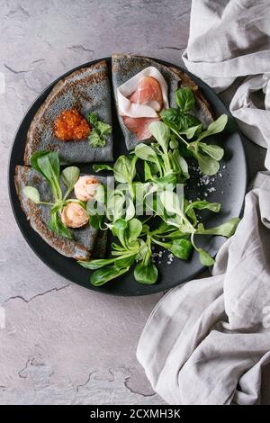 Crêpes crêpes noir avec variété de remplissage de sel caviar rouge, jambon, saumon pate de poisson, salade verte avec plus de serviettes linge textile texture gris backgrou Banque D'Images