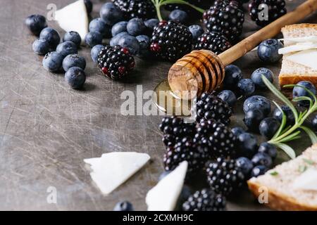 Les petits fruits, miel de bleuet et de blackberry sur balancier, romarin, des tranches de fromage de chèvre avec du pain servi plus de métal gris texture background. Sandwich de l'été. Banque D'Images