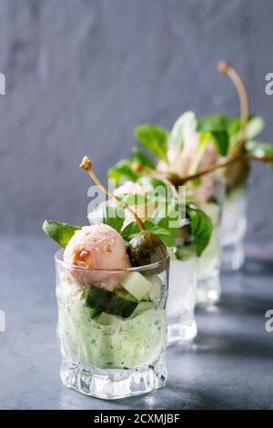 Verrines apéritif avec du saumon pate, caviar rouge, concombre, fromage à la crème, les herbes, les câpres dans les verres servis plus gris bleu texture background. Banque D'Images