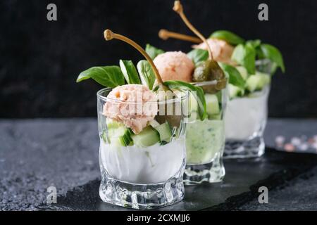 Verrines apéritif avec du saumon pate, caviar rouge, concombre, fromage à la crème, les herbes, les câpres dans les verres servis avec du sel rose et basilic sur noir ardoise Banque D'Images