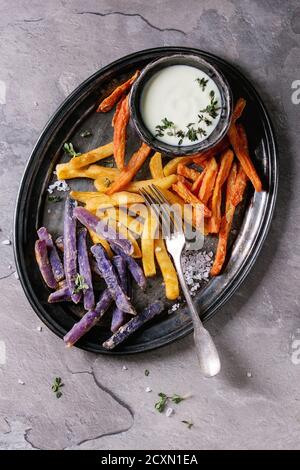 Variété de pommes de terre traditionnelles frites de pommes de terre, carotte pourpre, servi avec sauce au fromage blanc, le sel, le thym sur plateau vintage gris au dos de texture Banque D'Images