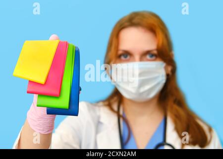 Femme médecin tient des bandes élastiques de forme physique sur un fond bleu, gros plan. Banque D'Images