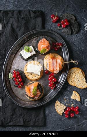 Pile de charbon noir et craquelins traditionnels avec le saumon fumé, fromage à la crème, salade verte et rouge des baies de cassis sur le plateau métallique vintage blac sur Banque D'Images