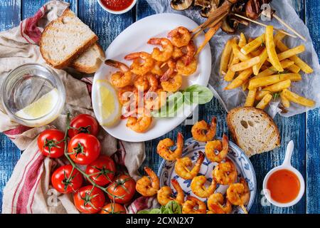 Variété d'installations pour barbecue. Épicé grillé plaques brochette de gambas king, brochettes de champignons, pain, pommes de terre frites, des tomates avec des sauces et les verts o Banque D'Images