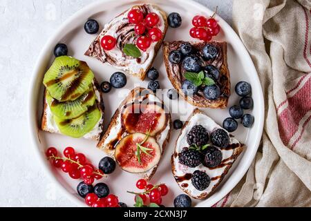 Variété de sandwichs dessert aux fruits rouges et crème de fromage et tourbillon de chocolat. De groseille rouge, de bleuets, de tranches de Kiwis, Figues en plaque blanche sur gray Banque D'Images