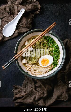 Bol de soupe asiatique avec nouilles soba au thé vert, œuf, champignons, oignon de printemps et tofu, servi avec des baguettes et une cuillère blanche sur sackclot Banque D'Images