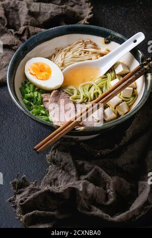 Bol de soupe asiatique avec nouilles soba au thé vert, bœuf, œuf, champignons, oignon de printemps et tofu, servi avec des baguettes et une cuillère blanche sur sa Banque D'Images