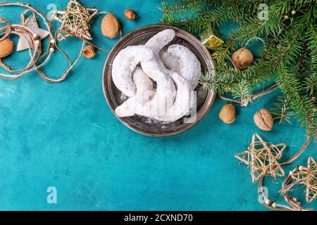 Biscuits aux noix de Noël faits maison croissant de sucre en poudre dans la décoration de vacances et sapin sur la surface de texture en bois turquoise avec espace de copie. Haut Banque D'Images