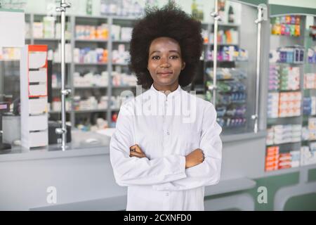Pharmacie, concept de soins de santé. Jeune femme africaine à la peau sombre et souriante pharmacien en manteau blanc, debout à l'intérieur de l'hôpital moderne Banque D'Images