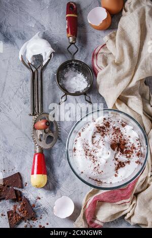 Ingrédients et ustensiles pour la cuisson de la meringue. Les blancs d'oeufs fouettés, le sucre en poudre, oeufs cassés, vintage et tamis mélangeur de main sur lin gris serviette sur te Banque D'Images