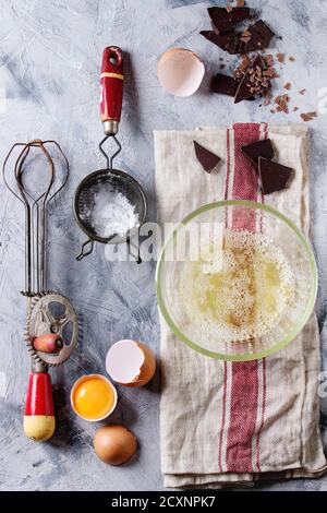 Ingrédients et ustensiles pour la cuisson de la meringue. Les blancs d'oeufs fouettés, le sucre en poudre, oeufs cassés, vintage et tamis mélangeur de main sur lin gris serviette sur te Banque D'Images