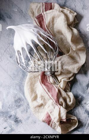 Processus de cuisson de la meringue. Blancs d'œufs fouettés sur le batteur fouetter sur une serviette de lin sur fond de texture grise. Vue de dessus. Concept de dessert de boulangerie Banque D'Images