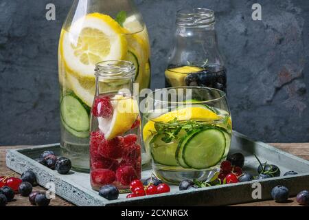 Agrumes concombres baies myrtille et framboise Sassy eau sassi pour le détox dans des bouteilles en verre sur fond bleu bois. Manger propre, vie saine Banque D'Images