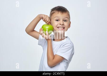 Mignon garçon tient une pomme verte devant son visage. Séance de photo dans le Studio sur un fond blanc Banque D'Images