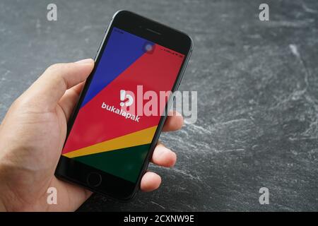 Mataram, Indonésie - 1 octobre 2020: Main tenant Apple iPhone 8 avec bukalapak Marketplace magasin en ligne sur l'écran sur la dalle de pierre, vue de dessus. Banque D'Images