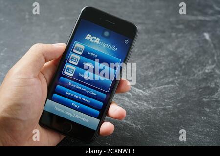 Mataram, Indonésie - 1 octobre 2020 : main tenant Apple iPhone 8 avec BCA mobile Bangking application sur l'écran de pierre, vue du dessus. Banque D'Images