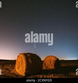 Meteor et Comet Neowise C2020 F3 dans Starry Sky de nuit au-dessus de Haystacks dans le champ agricole d'été. Étoiles de nuit au-dessus du paysage rural avec balles de foin Banque D'Images