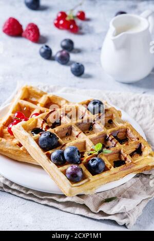 Petit-déjeuner avec gaufres belges carrées faites maison, baies fraîches mûres, myrtille, cassis, sauce balsamique sur plaque blanche avec verseuse de mi Banque D'Images