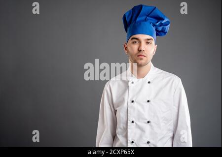 Portrait d'un jeune habillé d'un costume blanc de chef posant sur fond gris avec zone publicitaire de l'espace de copie Banque D'Images