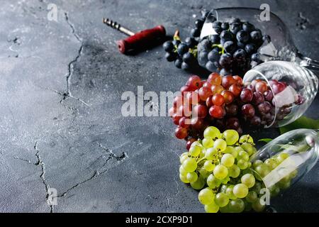 Variety of three type fresh ripe grapes dark blue, red and green in different lying wine glasses with old corkscrew over black texture background with Banque D'Images