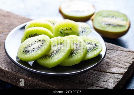 Tranches de kiwi dans un bol sur fond blanc foncé. Banque D'Images