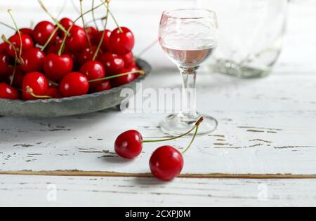 Boisson alcoolisée à la cerise Kirsch ou Kirschwasser - dans un verre et cerise fraîche sur la table en bois blanc Banque D'Images