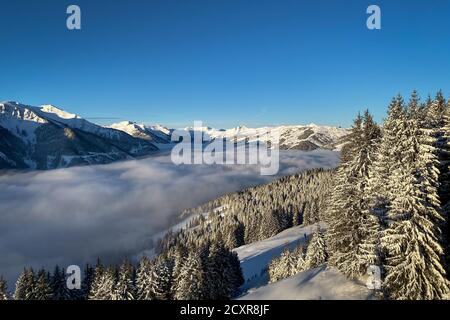 Vue panoramique sur les montagnes enneigées de la région de ski De Saalbach Hinterglemm dans les alpes autrichiennes sous une couverture de nuages contre ciel bleu dans le Banque D'Images