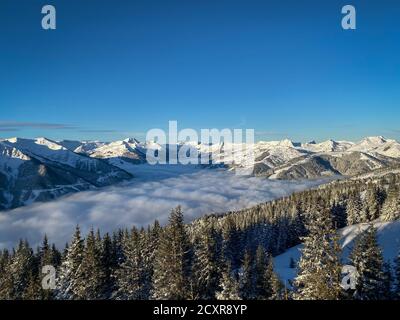 Vue panoramique sur les montagnes enneigées de la région de ski De Saalbach Hinterglemm dans les alpes autrichiennes sous une couverture de nuages contre ciel bleu dans le Banque D'Images