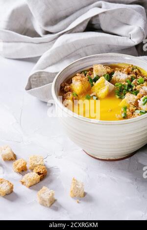 Tasse de soupe végétarienne de carottes à la citrouille servie avec des croûtons et des oignons sur une serviette en tissu sur fond de béton gris. Gros plan Banque D'Images