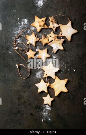 Guirlande de sablés faits maison star shape sugar cookies autre taille sur le filetage avec du sucre en poudre sur la surface texture sombre. Noël backgrou Banque D'Images