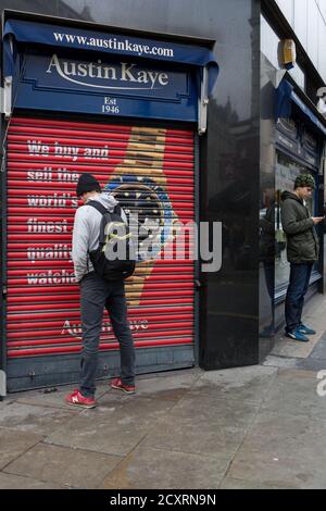 Un homme tient un bijoutier fermé dans la région de la ville de Chine se concentrant sur son téléphone mobile. Le quartier de Soho dans le West End de Londres lors d’une journée froide et humide de janvier. Banque D'Images