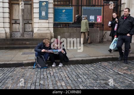 Les touristes s'assoient sur le trottoir à l'extérieur de l'église St Paul à Covent Garden en lisant une carte le West End de Londres lors d'une journée froide et humide de janvier. 31 janvier 2016. Pho Banque D'Images