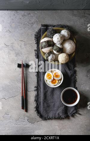 Bol avec différentes tailles de boules de riz et sésame noir avec des Algues Nori, servi avec des œufs durs, de la sauce de soja, des baguettes sur le tableau gris. Asian sty Banque D'Images