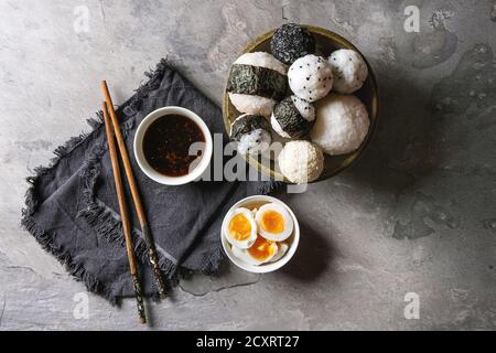 Bol avec différentes tailles de boules de riz et sésame noir avec des Algues Nori, servi avec des œufs durs, de la sauce de soja, des baguettes sur le tableau gris. Asian sty Banque D'Images