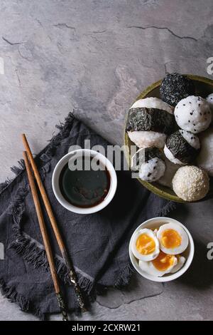 Bol avec différentes tailles de boules de riz et sésame noir avec des Algues Nori, servi avec des œufs durs, de la sauce de soja, des baguettes sur le tableau gris. Asian sty Banque D'Images