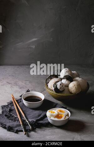 Bol avec différentes tailles de boules de riz et sésame noir avec des Algues Nori, servi avec des œufs durs, de la sauce de soja, des baguettes sur le tableau gris. Asian sty Banque D'Images