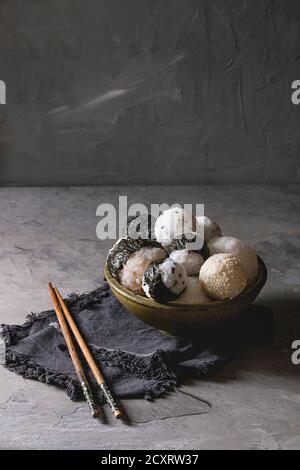 Bol avec différentes tailles de boules de riz et sésame noir avec des Algues Nori, servi avec des œufs durs, de la sauce de soja, des baguettes sur le tableau gris. Asian sty Banque D'Images