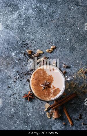 Tasse en verre de thé chai masala indien traditionnel avec des ingrédients ci-dessus. Cannelle, cardamome, l'anis, le sucre, le thé noir sur fond texture sombre. Haut Banque D'Images