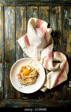 Traditionnel italien Pasta alla carbonara avec oeuf, bacon pancetta, parmesan, thym, servi en plaque blanche sur lin textile plus ancienne en bois pla Banque D'Images