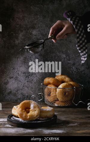 Beignets faits maison avec du sucre en poudre par aspersion en grille vintage enfant part sur noir servant de sélection et en panier sur la vieille planche en bois table. Dar Banque D'Images