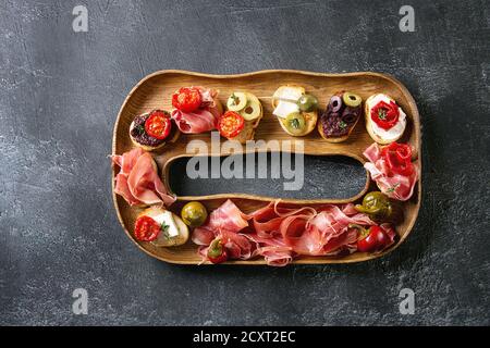 Des tapas ou bruschetta variété. Pain croustillant avec du jambon prosciutto, tomates séchées, huile d'olive, olives, poivre sur plaque de bois décoratif sur un texte foncé Banque D'Images