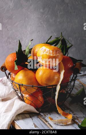 Clémentines ou mandarines biologiques mûrs avec des feuilles dans panier debout avec cuisine serviettes sur la planche en bois blanc table avec mur gris en arrière-plan. Rus Banque D'Images