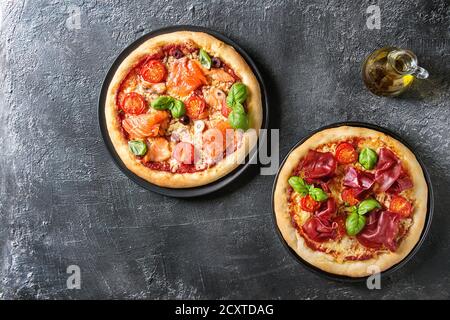 Deux pizza traditionnelle avec bresaola, saumon fumé, fromage, tomates et basilic servi sur les plaques noires avec de l'huile d'olive sur fond texture noire. À Banque D'Images