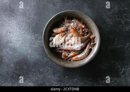 Crevettes entières fraîches non cuites crues sur glace dans un bol en métal vintage sur fond de texture noire. Vue de dessus avec espace de copie Banque D'Images