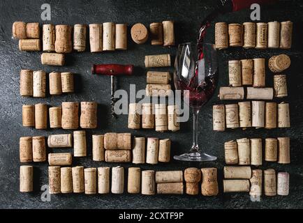 Grand ensemble de bouchons de vin utilisés en rangées avec un tire-bouchon vintage et verser le vin rouge dans le verre sur fond de texture noire. Vue de dessus. Banque D'Images