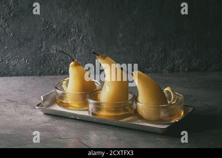 Dessert traditionnel confit de poires au vin blanc servi dans des bols en verre avec le sirop et les zestes de citron sur la texture gris table. Banque D'Images