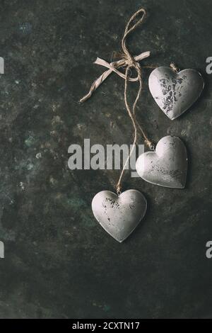 Carte de vœux Love Valentines Day avec trois coeurs argentés sur corde sur fond vieux métal foncé. Vue de dessus, espace de copie. Image en tons Banque D'Images