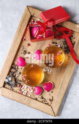 L'amour Saint Valentin carte de souhaits avec deux verres de thé chaud, boutons de rose, forme de coeur, composé de biscuits comme cadeau, rose sucre, thé passoire, ruban rouge o Banque D'Images